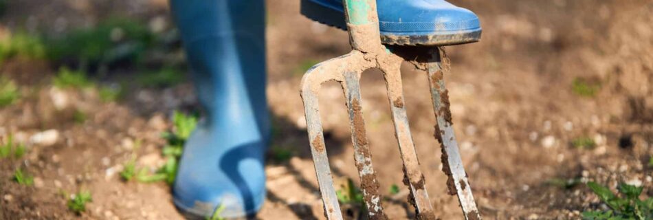 person in boots digging a garden fork nto soil