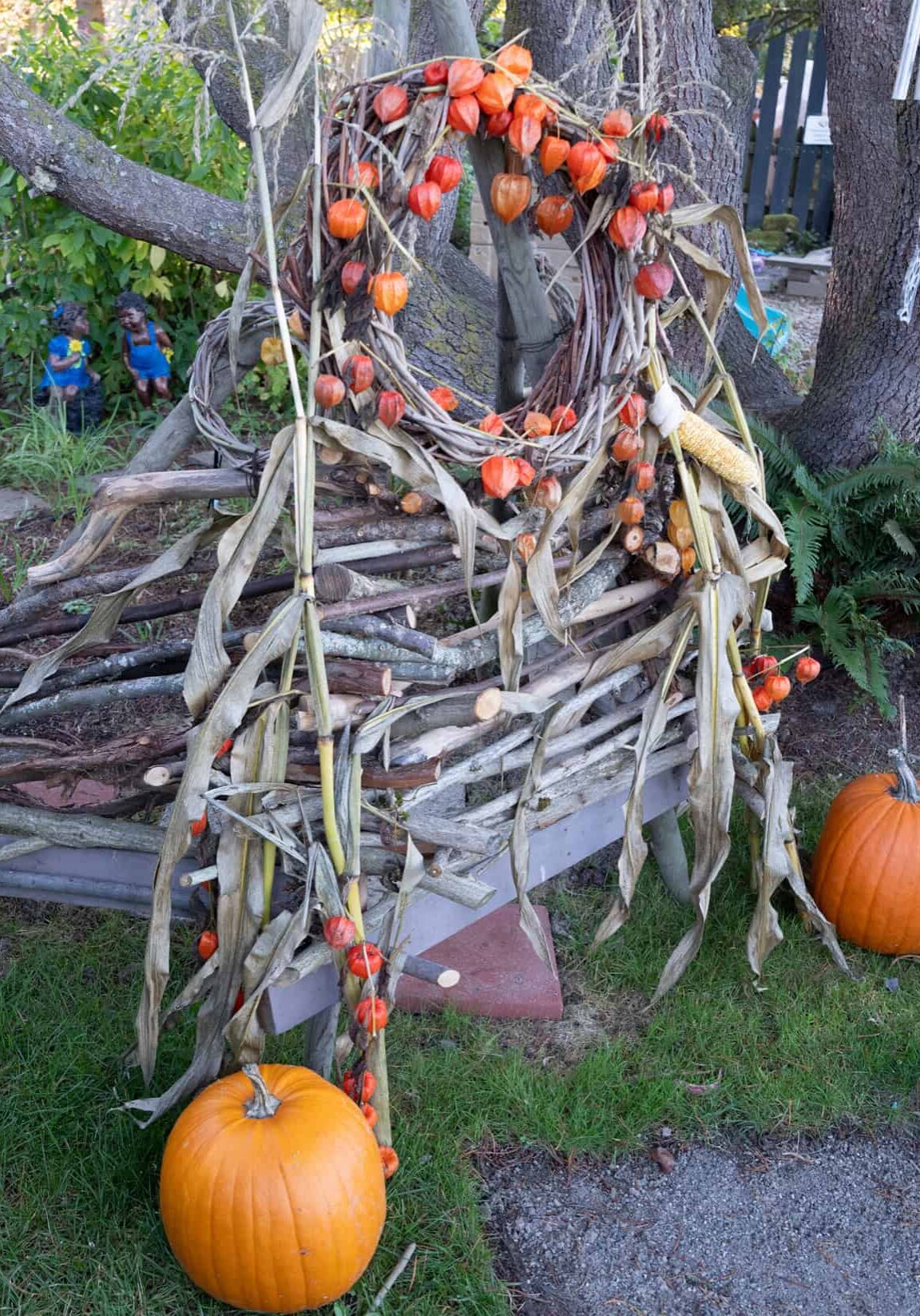 pumpkins in front of structure built of twigs and branches with a hole in middle for looking out.