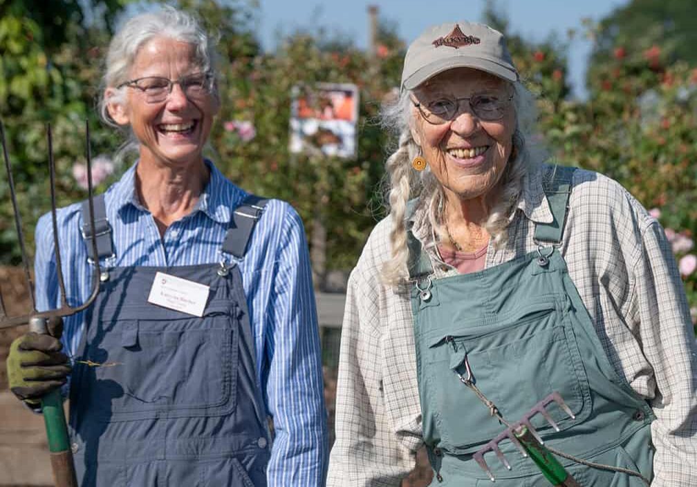 two smiling gardeners standing side by side wearing overalls